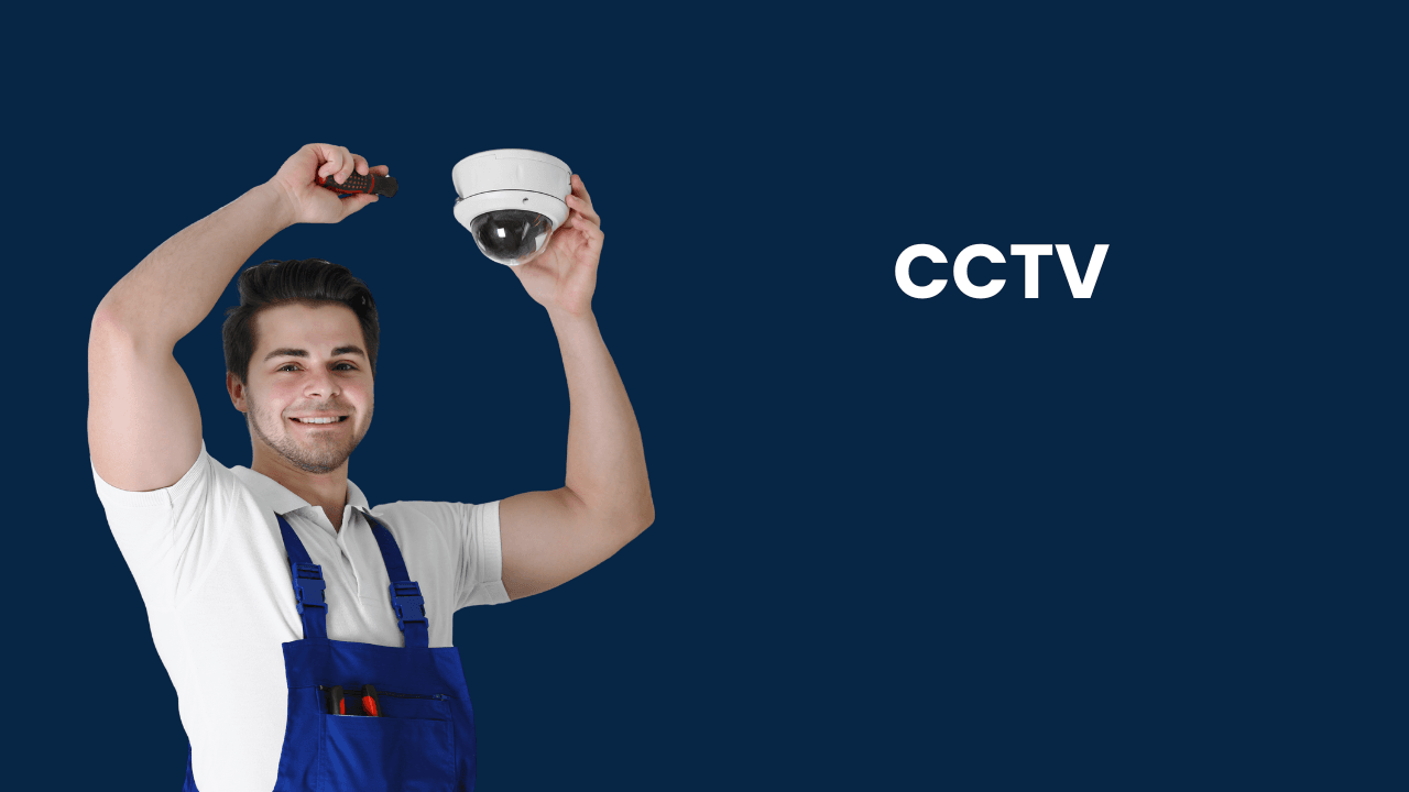 A man in a blue overall holding a CCTV camera while smiling at the camera.